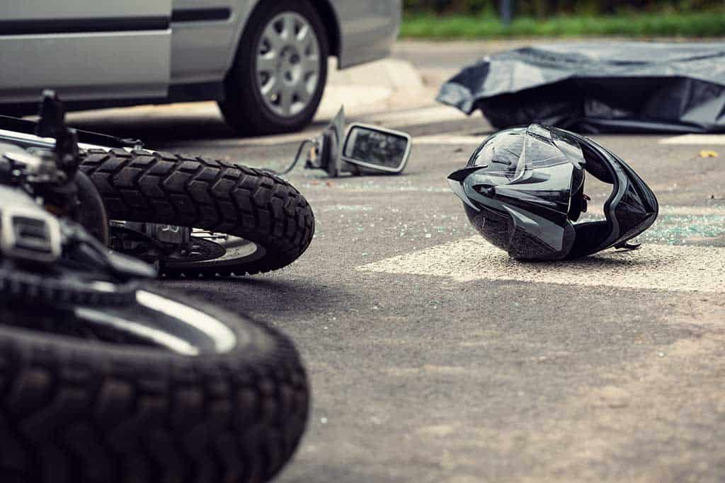 low view of street and auto accident with fallen motorcycle, motorcycle helmet, car debris, and car in the background